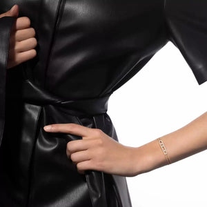 Close-up of a person adjusting the waistband of a black leather outfit on a white background wearing a gold bracelet
