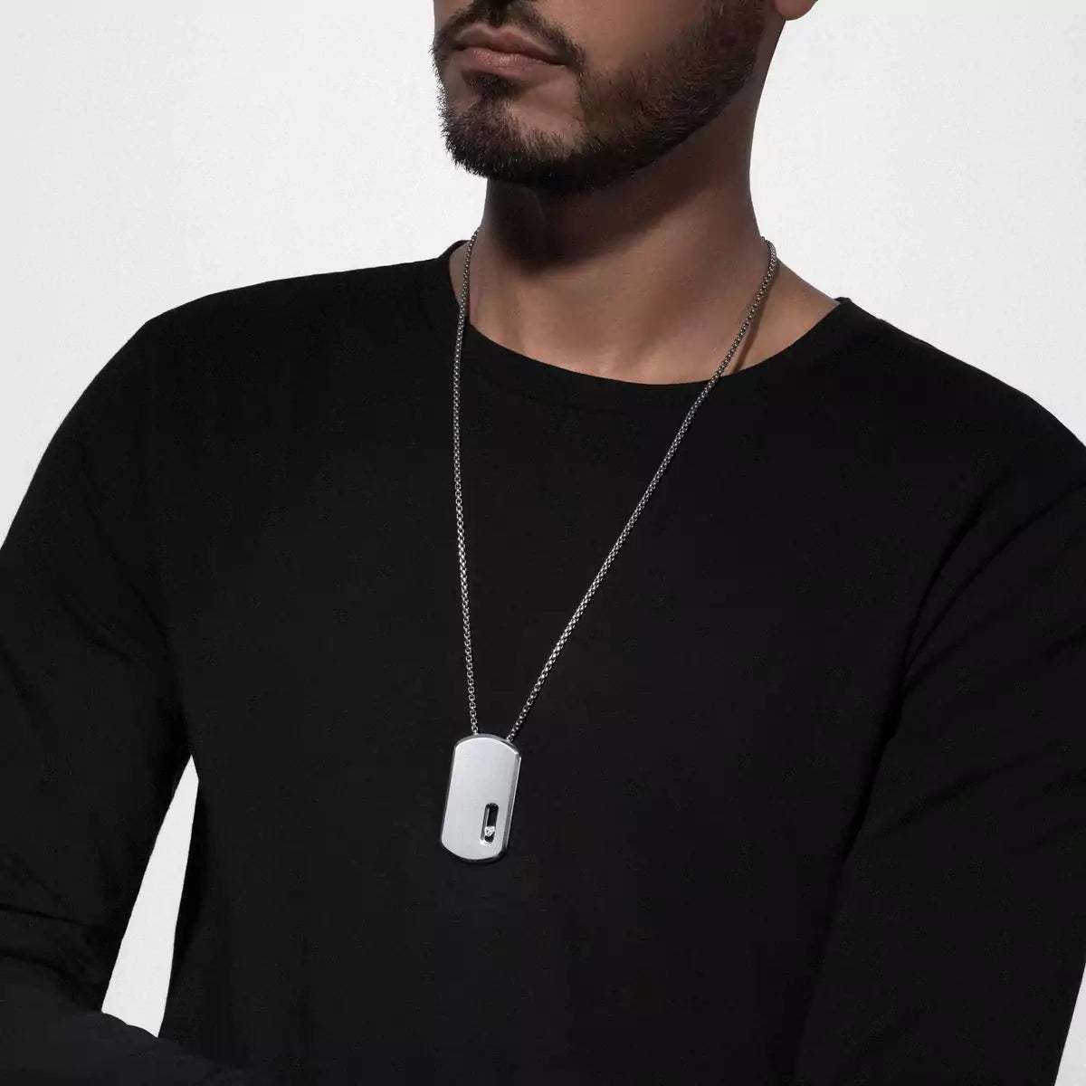 Man wearing a black shirt with a silver chain and dog tag necklace on a light gray background
