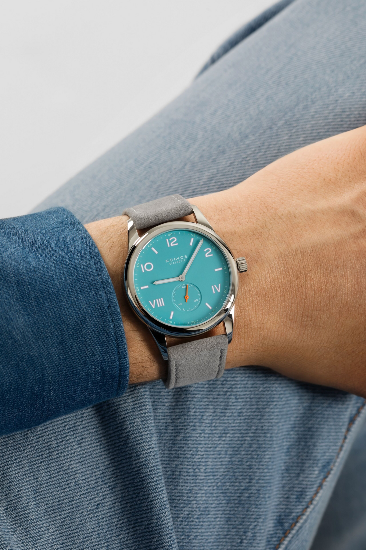 Wrist shot of Club Campus 38 watch showing endless blue dial and gray suede strap on a wrist resting on denim