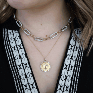 Close-up of 18K white and yellow gold 10.88ctw diamond pendant with halo layered over pave diamond link chain on black top