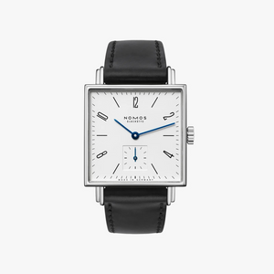 Nomos watch with black leather strap and white face on a light gray background