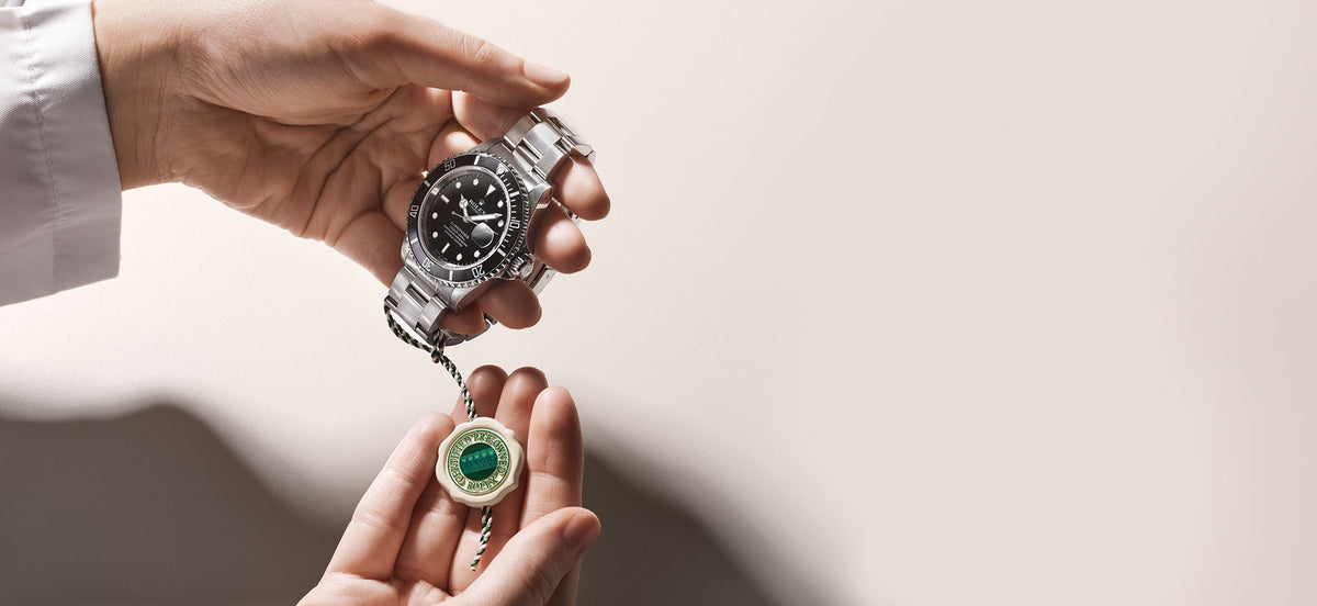 Angled view of stainless steel Rolex Submariner with black dial and cyclops date, held with certified pre-owned tag