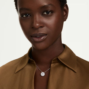 a model wearing a silver necklace with a round center stone on a white background