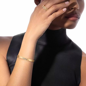 Person wearing gold bracelets and a ring on a plain background