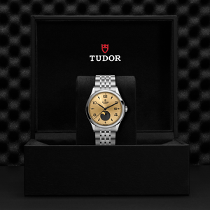 Front view of TUDOR 1926 Luna steel watch showing champagne dial with moon phase and steel bracelet in black Tudor box