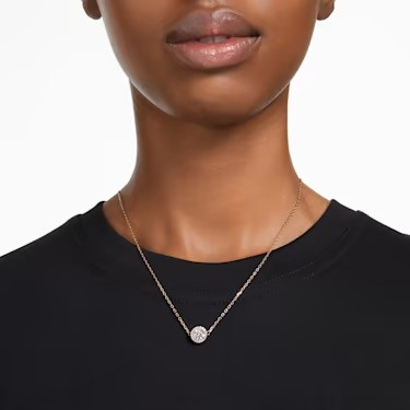 Front view of Constella pendant necklace, round halo pendant on rose gold chain at collarbone against black top