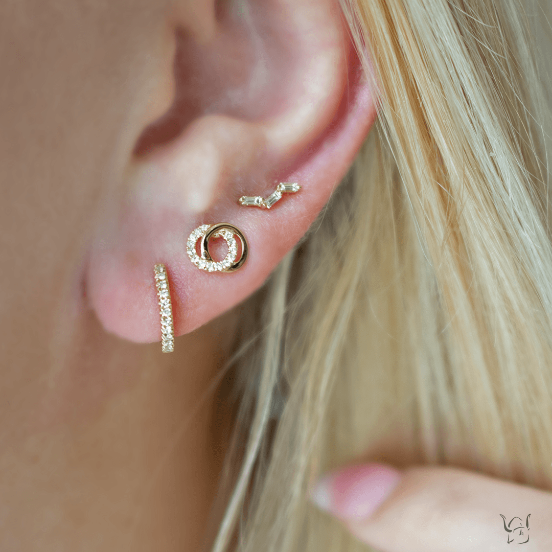 Close up of ear wearing 14K yellow gold huggie earring with 0.07 ctw diamonds, styled with two additional gold stacking earrings