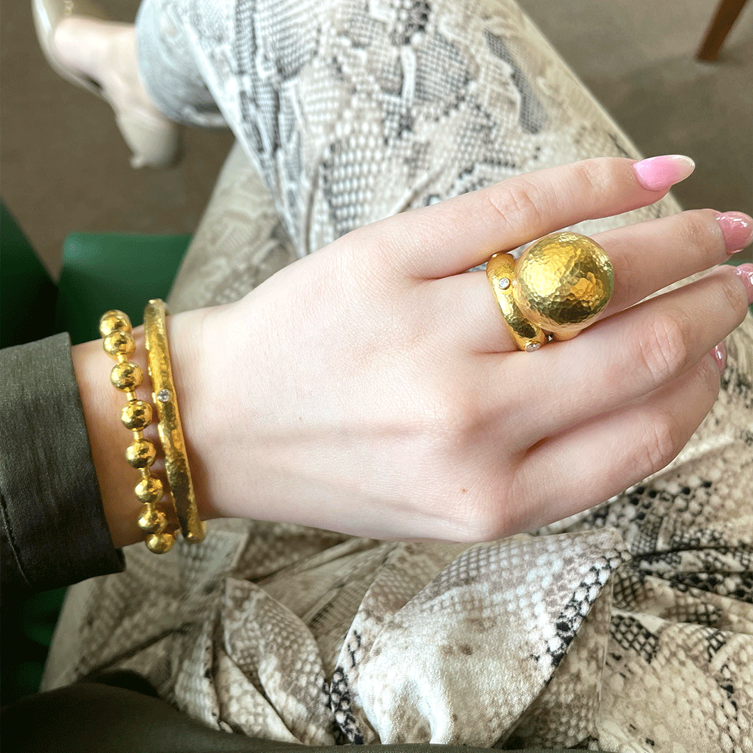 Close up of hand wearing gold and diamond band ring with hammered dome and small diamond on snakeskin pants
