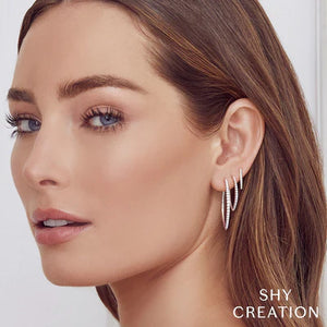 Woman wearing three diamond V hoop earrings; SHY CREATION logo at bottom right.