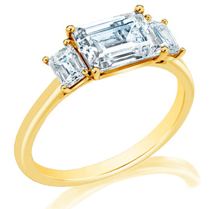 Angled view of 14K yellow gold engagement ring with emerald-cut center and two smaller emerald-cut side diamonds on white background