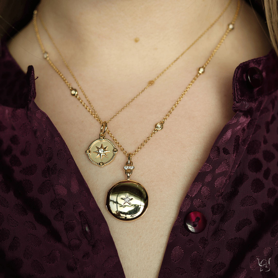 Front view of Mini Adventure compass charm in 18K yellow gold with white diamond, layered on model over burgundy shirt