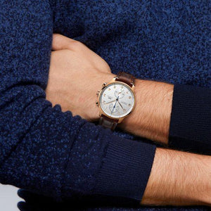 Wrist shot of Portugieser Chronograph showing 18 ct 5N gold case, silver chronograph dial, and brown leather strap against navy sweater sleeve