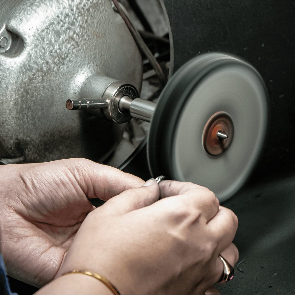 Jeweler's hands holding a ring against a spinning polishing wheel during rhodium plating preparation.