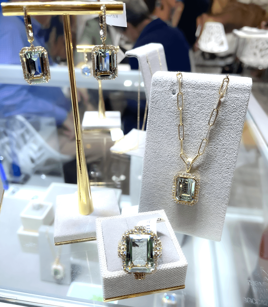 Gold chain necklace with emerald-cut green gemstone pendant, matching ring and earrings on white display stands.
