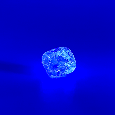 Cushion-cut diamond glowing bright blue under ultraviolet light on a deep-blue background