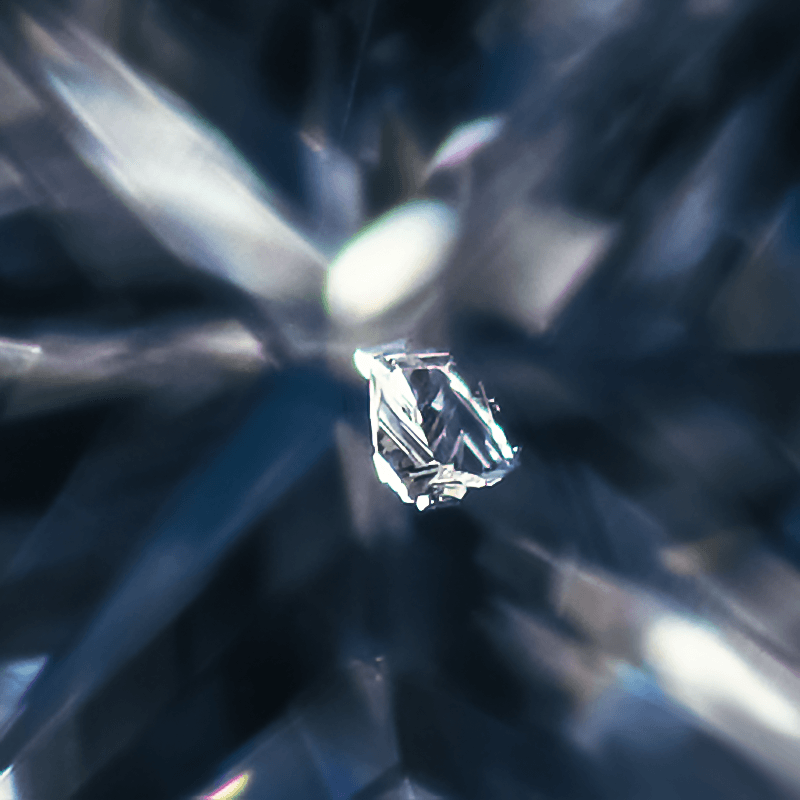 Macro of a small crystal inclusion inside a faceted diamond, centered against blurred blue-gray facets
