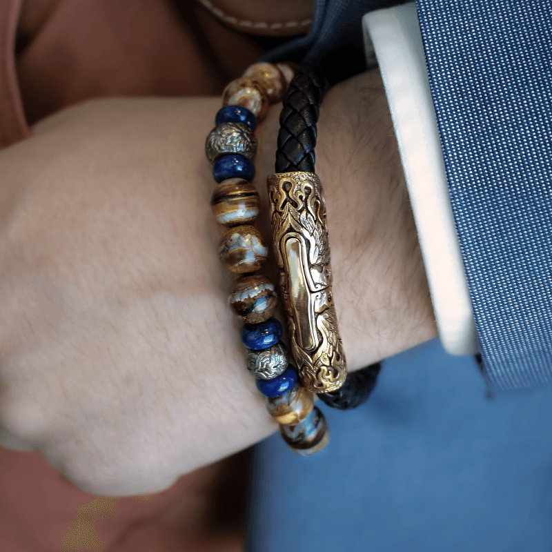Braided leather bracelet with ornate gold clasp and a blue-brown beaded bracelet on a wrist