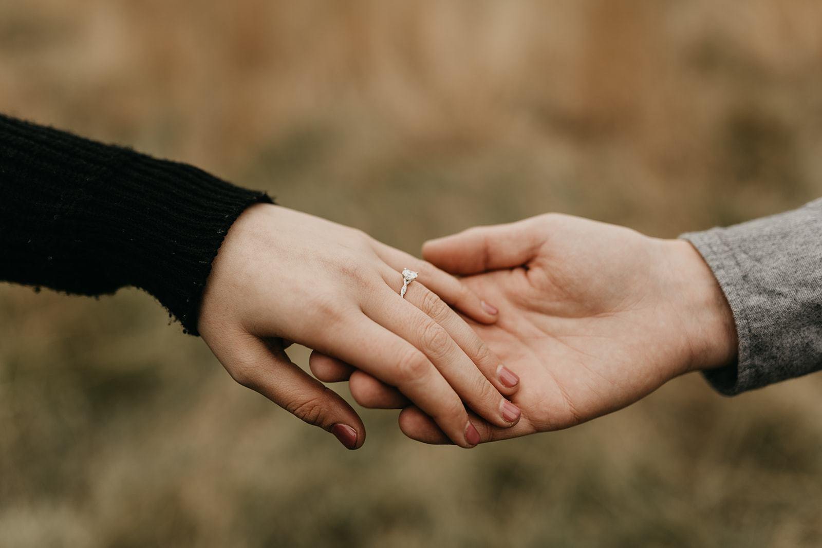 Close-up of two hands holding; solitaire diamond engagement ring on the left hand's ring finger