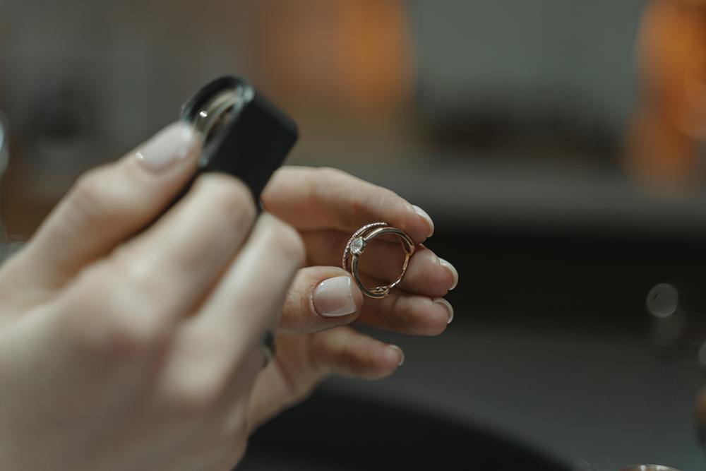Hands holding a diamond ring while a jeweler inspects it with a loupe, suggesting appraisal or repair.