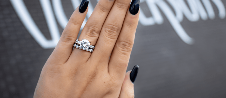 Hand with black manicure wearing a round-center diamond engagement ring and matching diamond bands