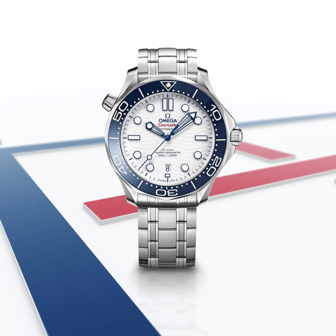 Front view of Omega Seamaster Co-Axial Master Chronometer 300m watch showcasing white wave dial, blue bezel, date at 6 o’clock and stainless steel bracelet on white background with red and blue accents