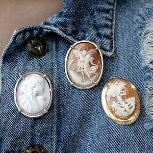 Three carved shell cameo brooches (two gold, one silver) pinned to a denim jacket, close-up view