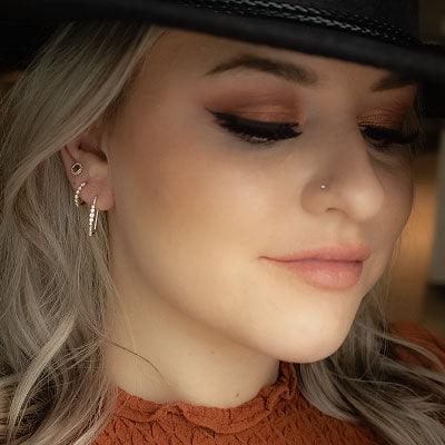 Close-up of left ear wearing three Shy Creation earrings with a heart stud, small hoop, and vertical diamond bar in soft light