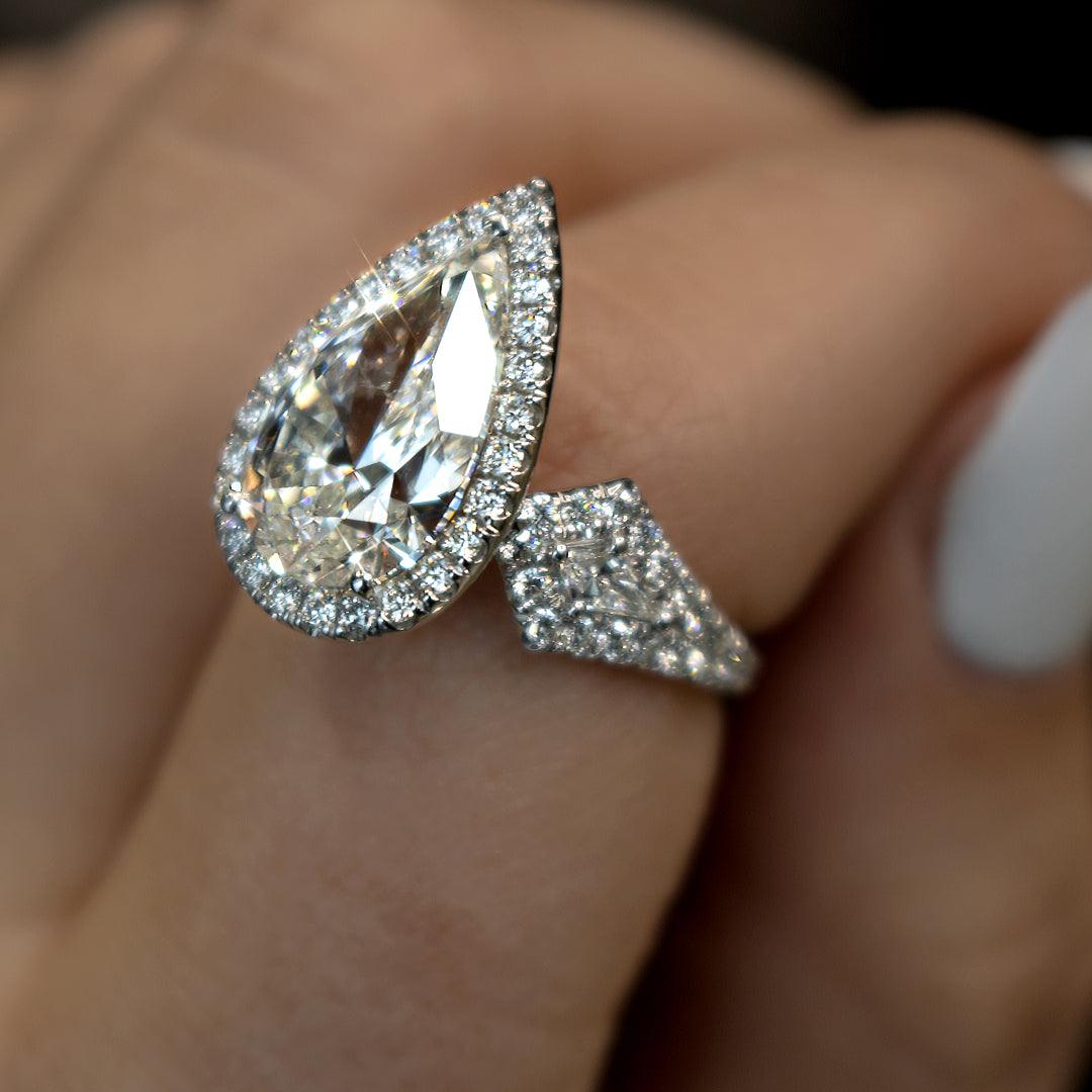 Pear-shaped diamond halo engagement ring with pavé diamonds, worn on a finger