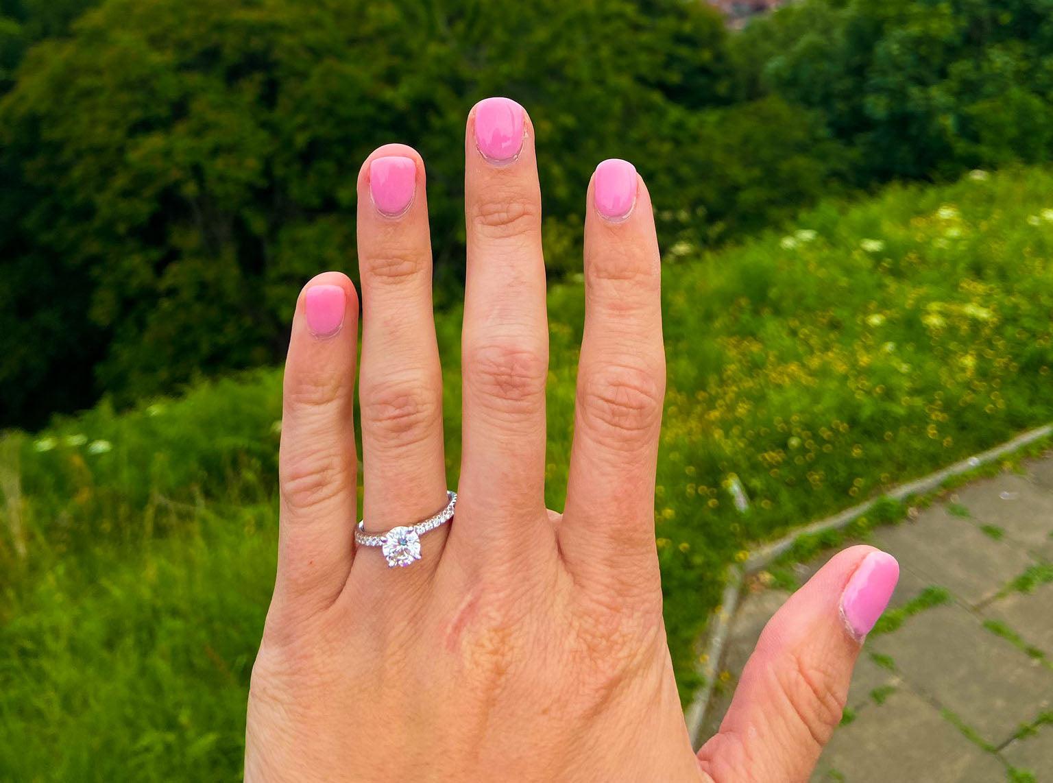 Left hand showing solitaire diamond engagement ring on ring finger with pink nail polish