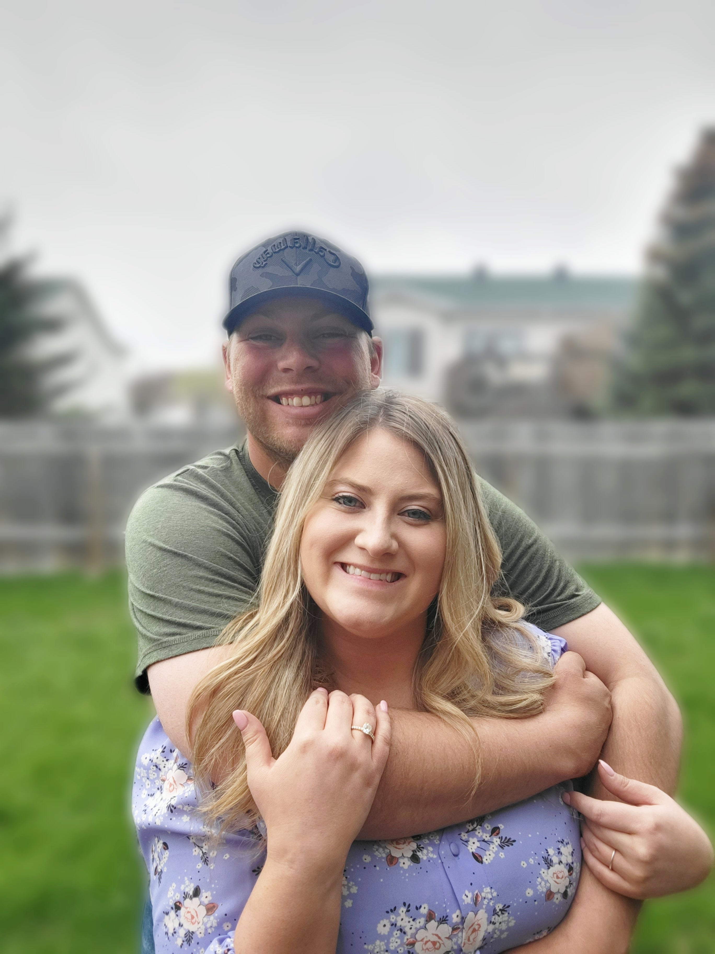 Hanna and Chandler smiling together in a backyard; Chandler wearing a Callaway cap and Hanna showing her engagement ring.