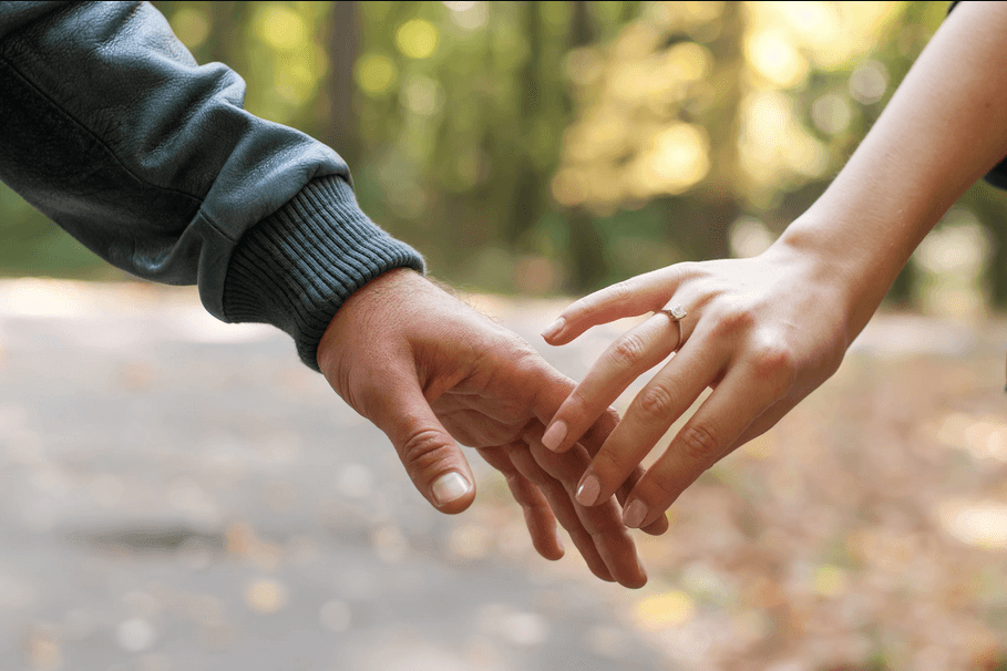 Tori and Austin reaching hands on a path; woman's left hand shows an engagement ring.