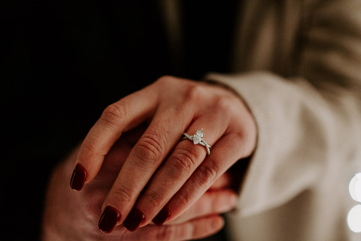 Close-up of marquise diamond engagement ring on a hand with red nails showing the center marquise stone and twisted pavé band