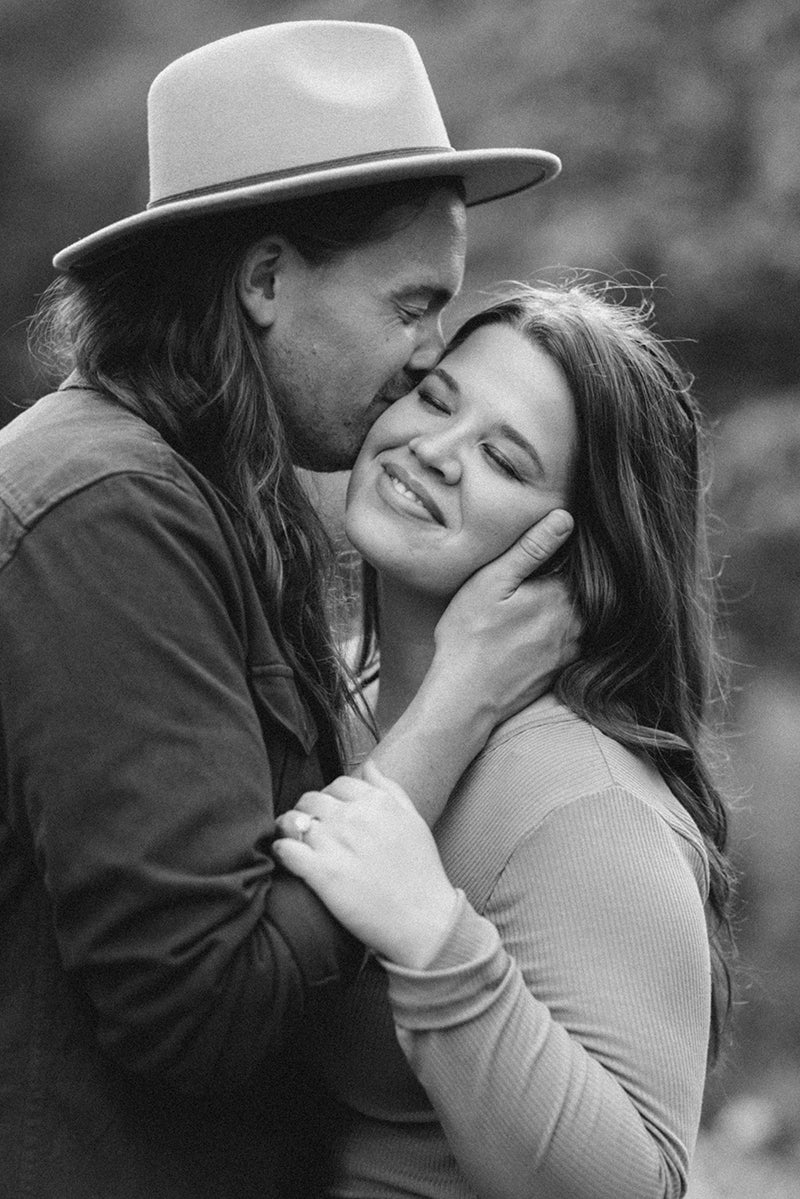 Megan and Michael embracing; Michael kisses Megan's temple as she smiles, her engagement ring visible on her left hand.