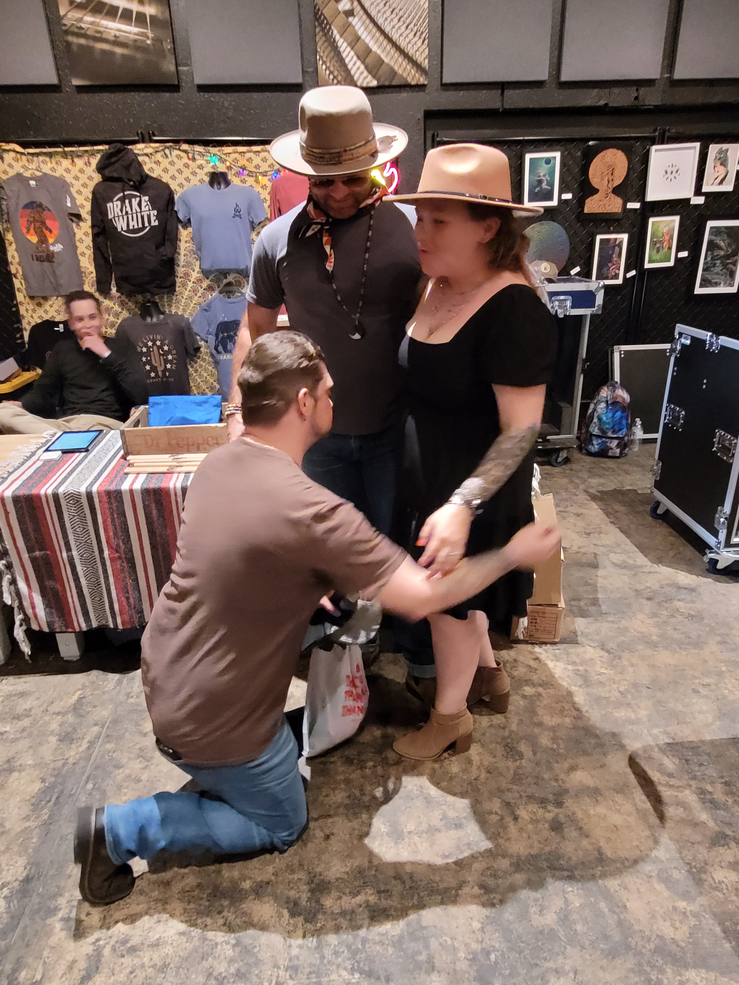 Kneeling man hugging standing woman with another man behind; background reads DRAKE WHITE and Dr Pepper.