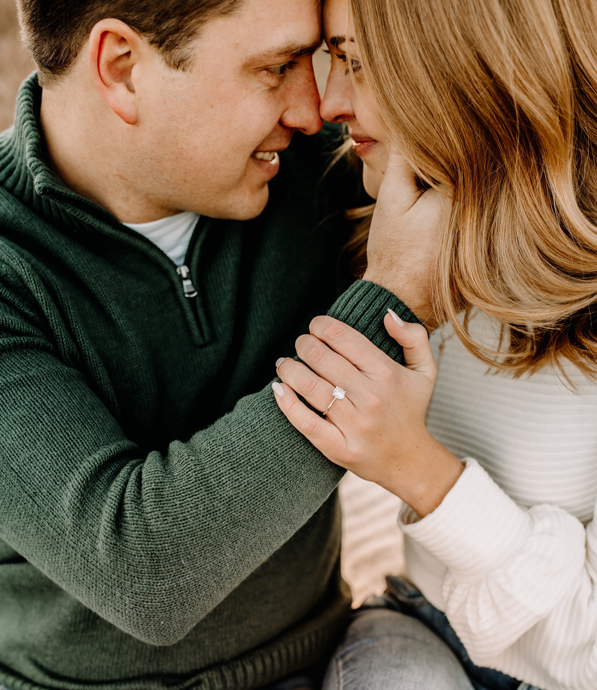 Couple touching foreheads, her hand on his arm showing a solitaire engagement ring