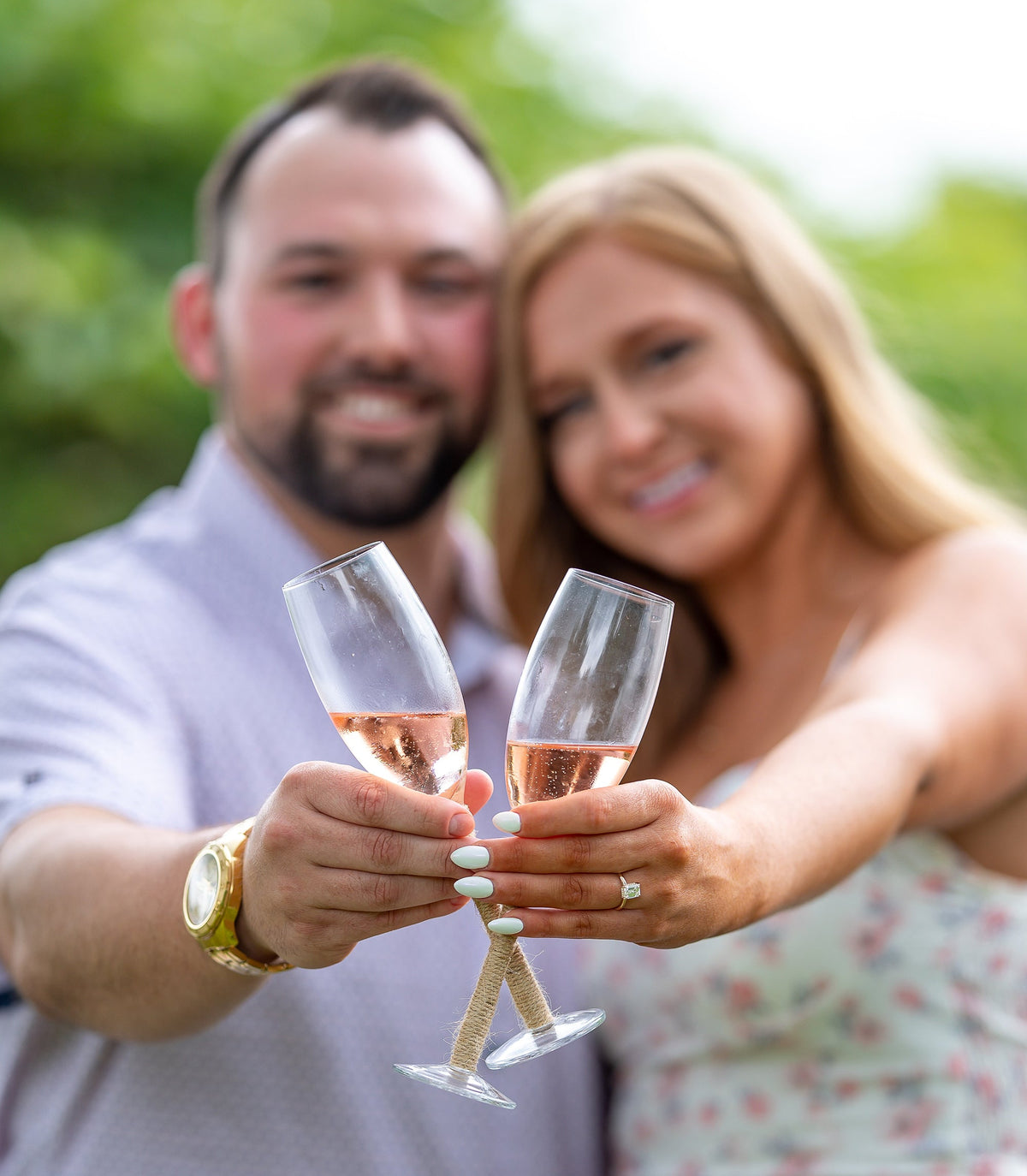 Couple toasting with champagne outdoors, close-up on hands showing the woman’s engagement ring