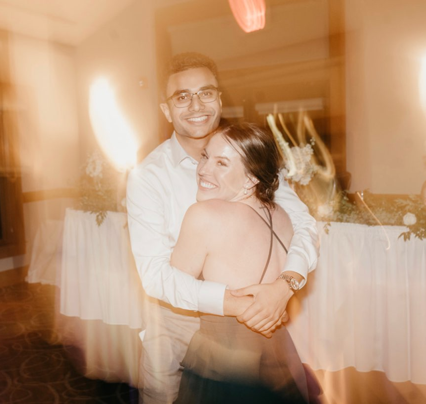 Couple hugging and smiling on a warmly lit wedding reception dance floor with motion-blur lights in the background