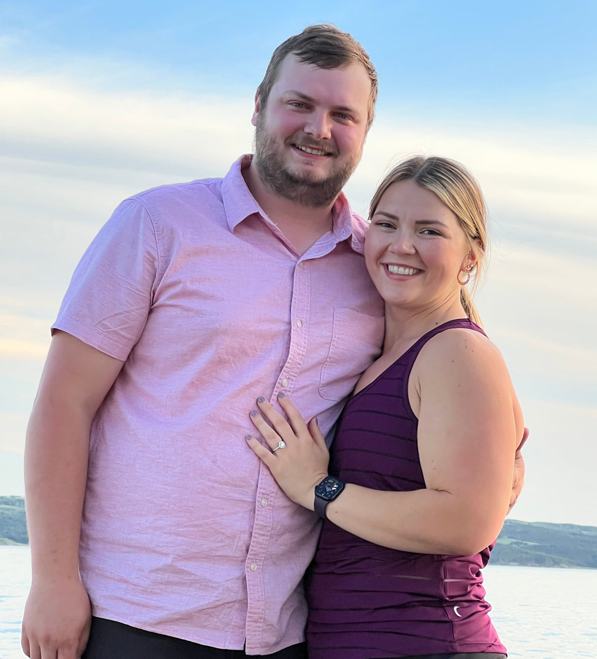 Smiling couple embracing on a boat at sunset with the woman’s engagement ring visible