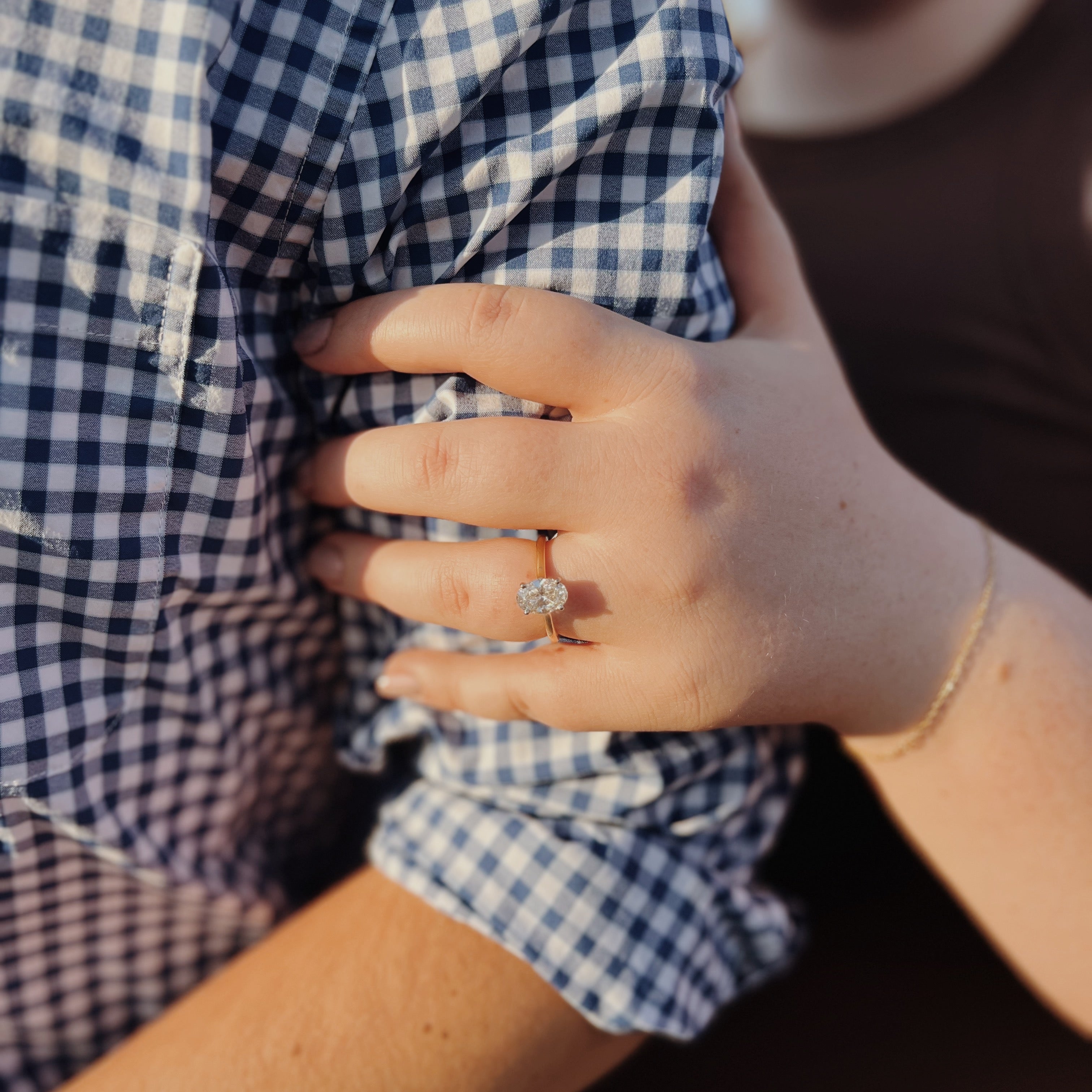Woman's hand with engagement ring resting on partner's blue gingham shirt sleeve