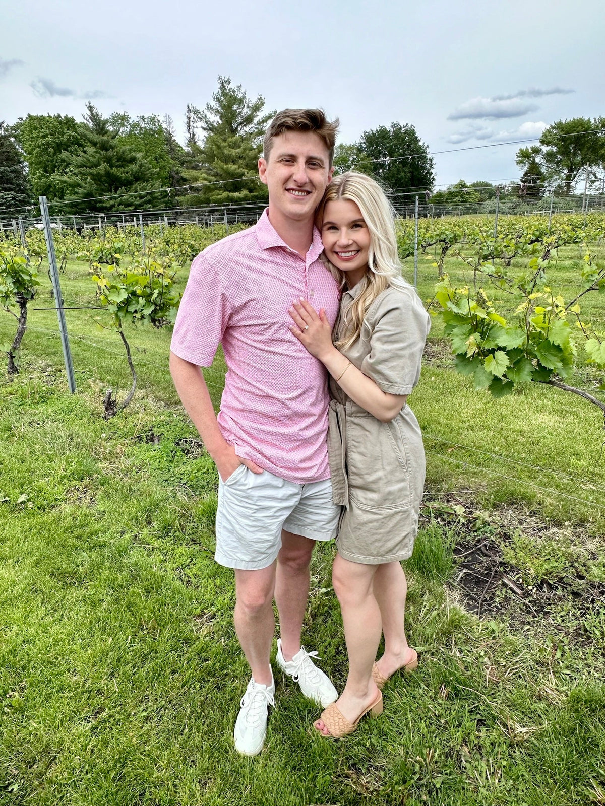 Young engaged couple smiling and embracing in a vineyard, woman showing her engagement ring