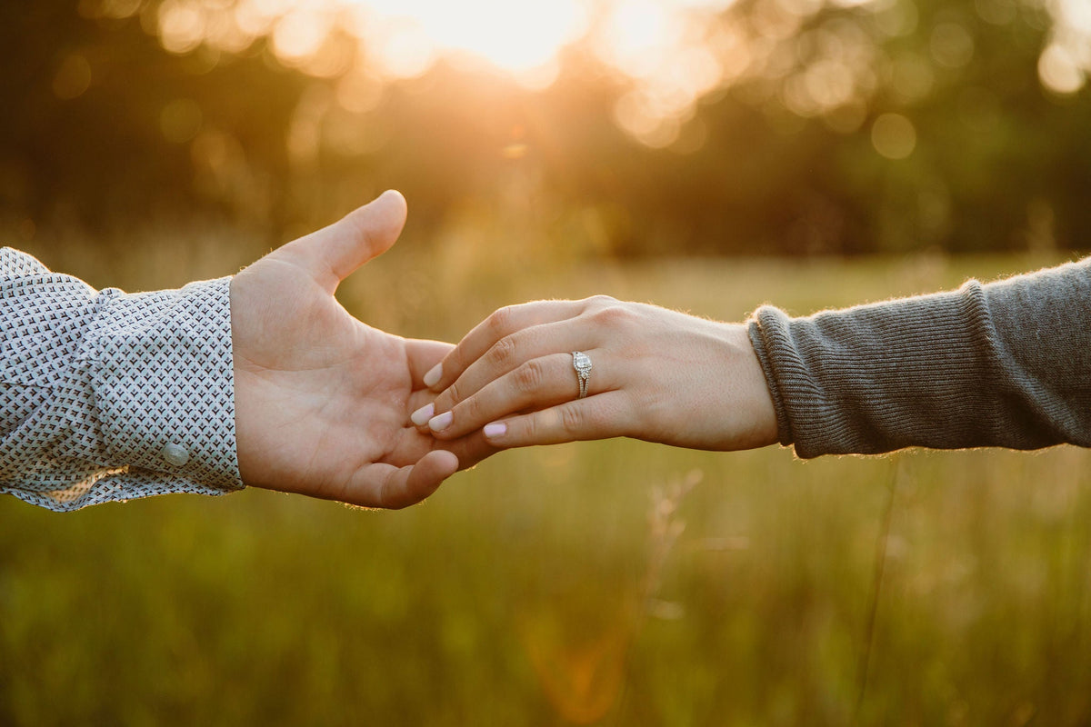 Two hands reaching at sunset, woman’s hand showing a cushion-cut customized white gold .91 carat engagement ring