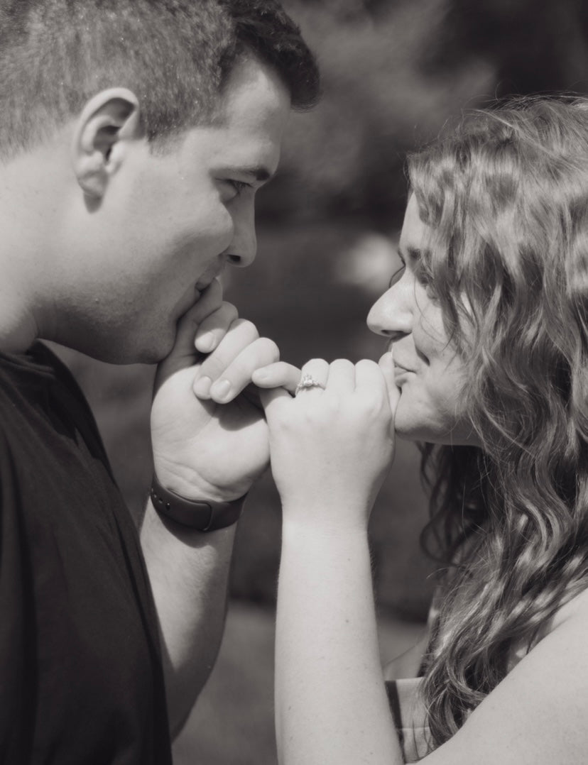 Couple touching pinkies, smiling face-to-face; woman wearing 1.07 ct pear center engagement ring in yellow gold outdoors