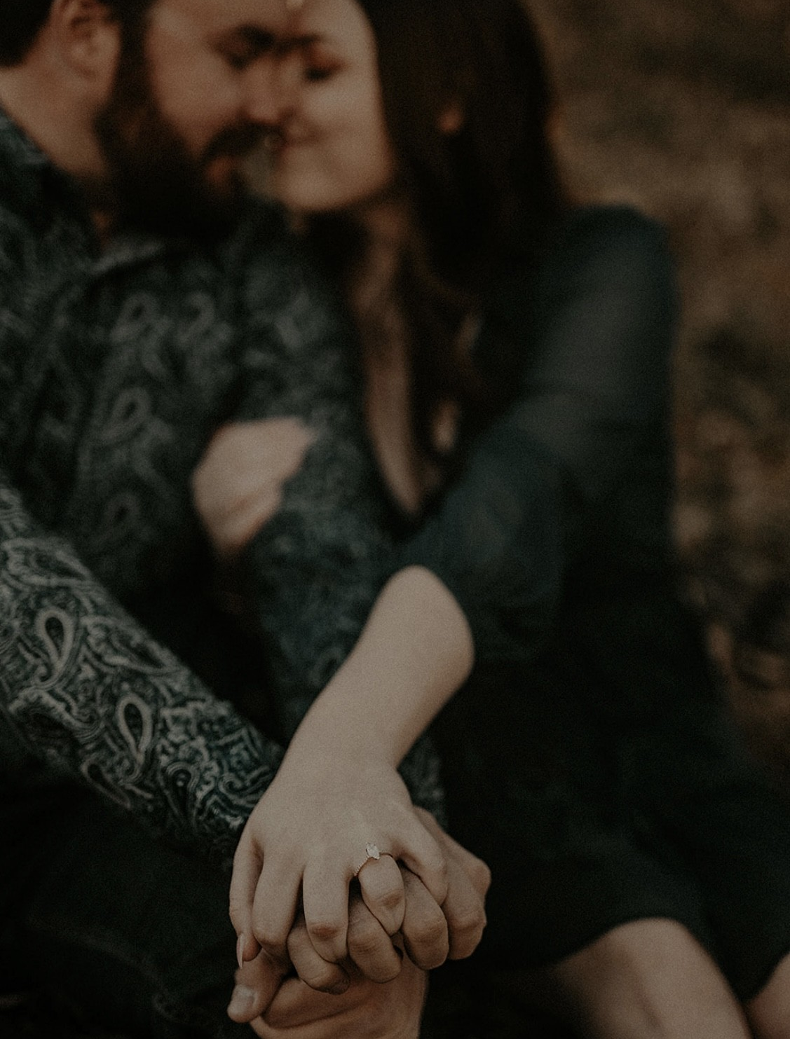Couple holding hands showing a marquise yellow gold engagement ring at Custer’s Peak with blurred outdoor background