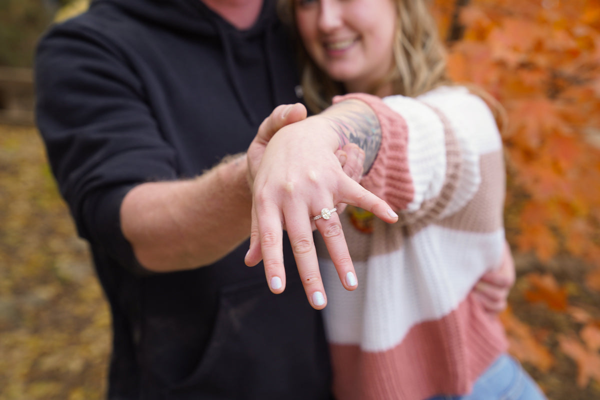 Woman showing her diamond engagement ring while embraced by her partner at an autumn pumpkin patch