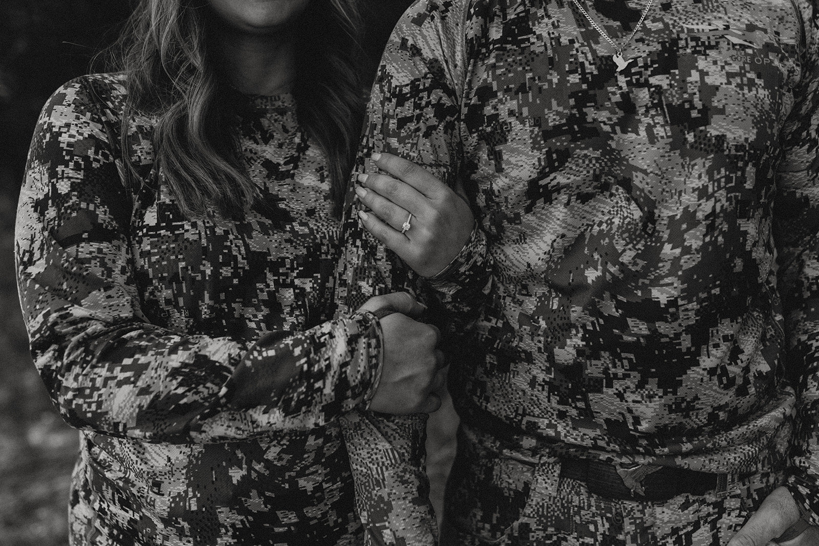 Ashley and Preston in matching camouflage shirts; she links his arm, showing an engagement ring on her left hand.