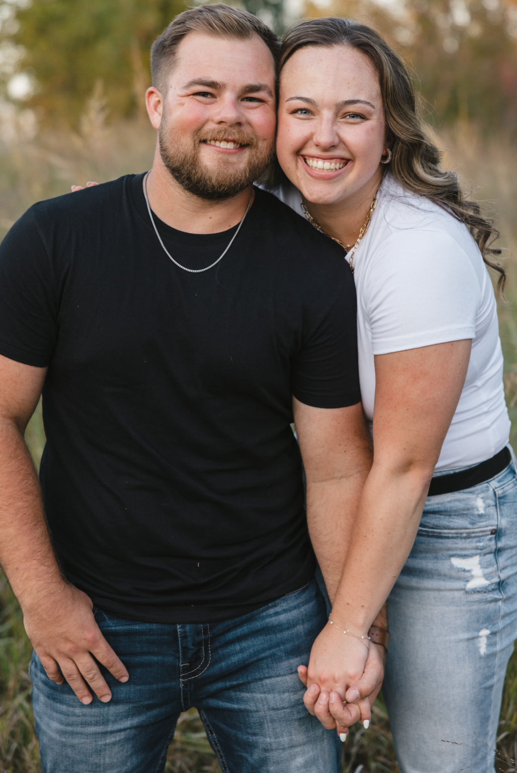 Couple smiling and holding hands in a grassy field at golden hour