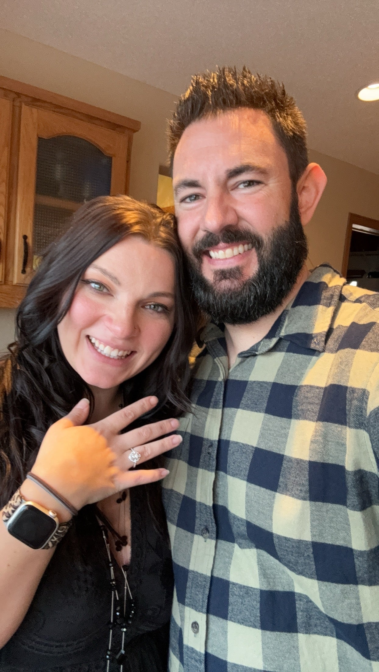 Newly engaged couple smiling while the woman shows her diamond engagement ring in a kitchen