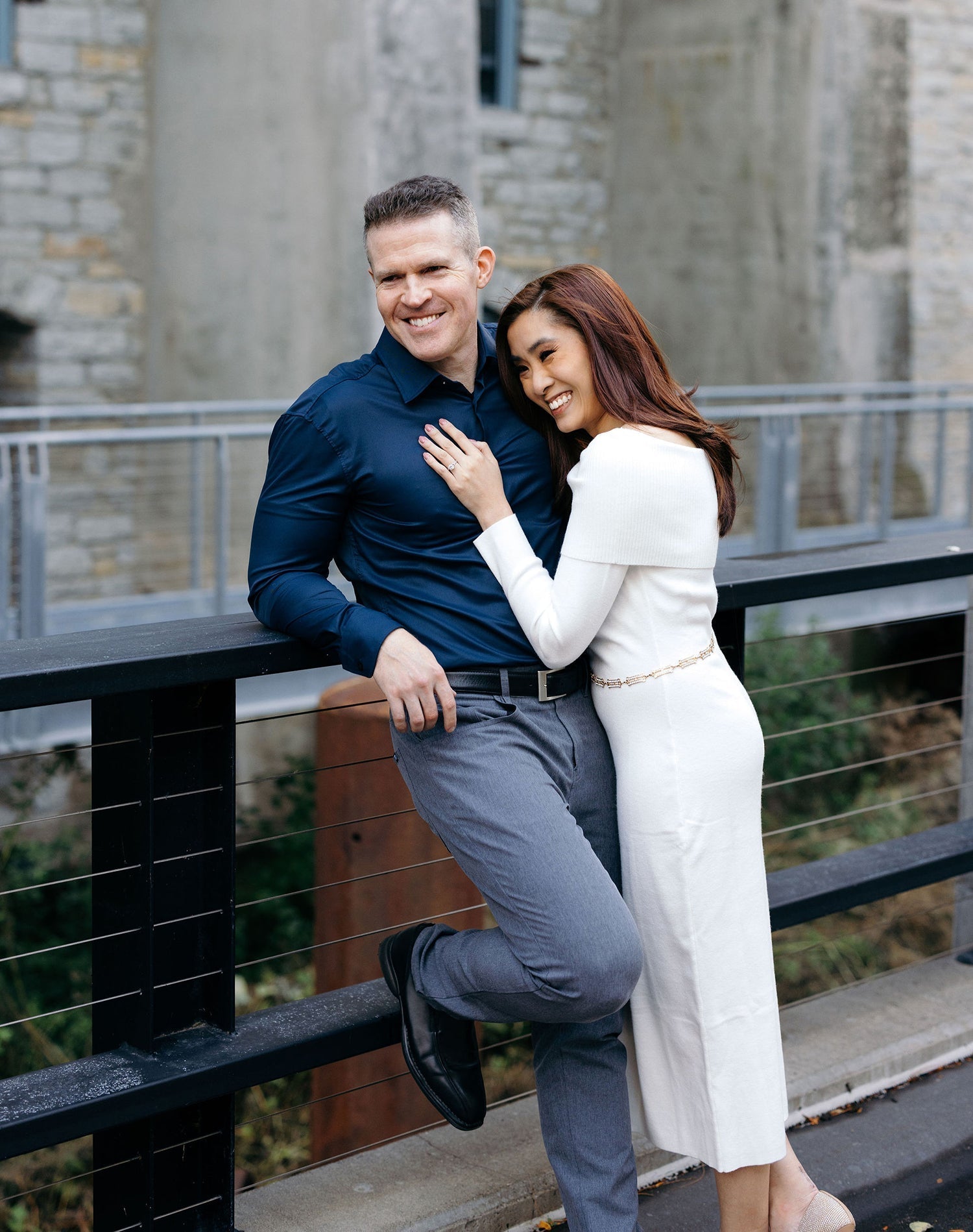 Pauleen and Todd smiling on a bridge, Pauleen leaning on Todd showing her engagement ring