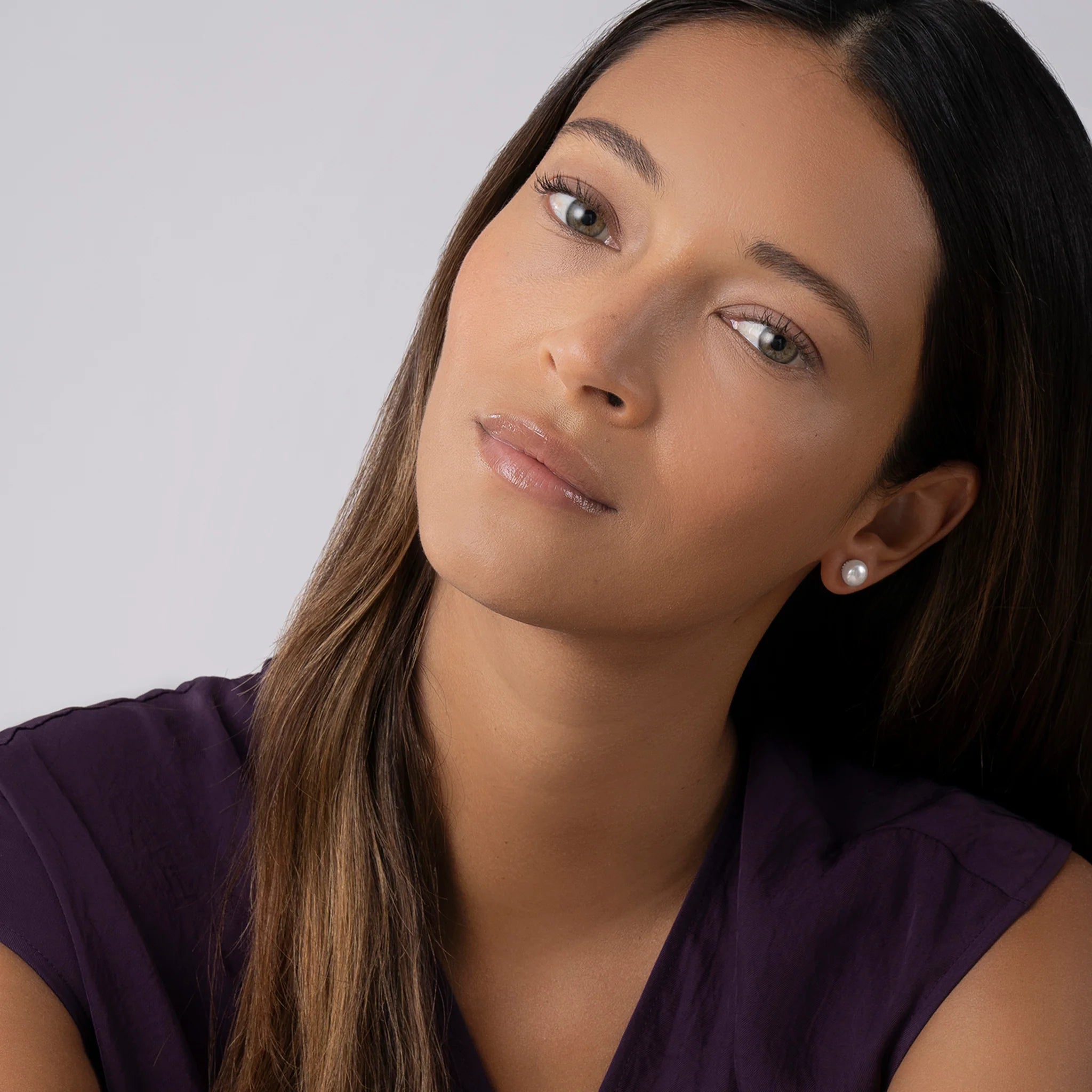 woman wearing purple shirt and pearl earrings on a grey background