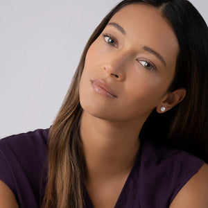 woman wearing purple shirt and pearl earrings on a grey background